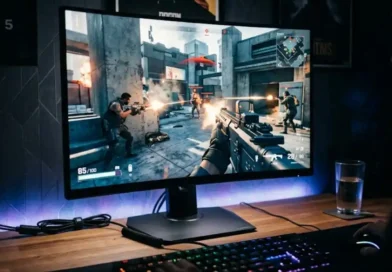 A gaming monitor with high refresh rate showing a fast-paced FPS game on a wooden desk inside a dimly lit gaming room with RGB lighting.