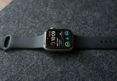 A modern smartwatch with a vivid AMOLED display showing a colorful watch face, placed on a dark matte surface with soft studio lighting highlighting the screen's deep blacks and bright colors.